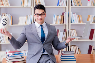 Businessman in library with a money sack and a laptop