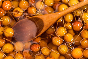 A wooden spoon lies in a bowl with apples in syrup.