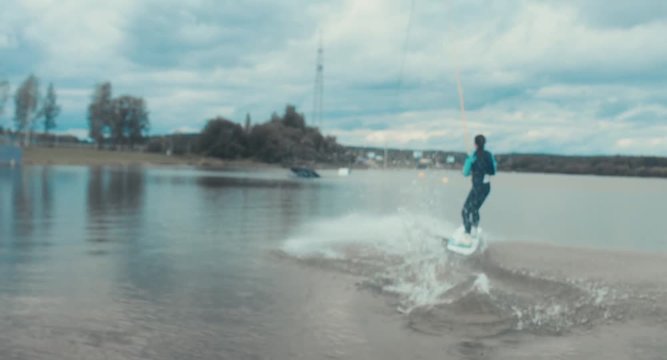 Attractive female wake boarding in a wakepark near a city. 4K UHD 60 FPS 