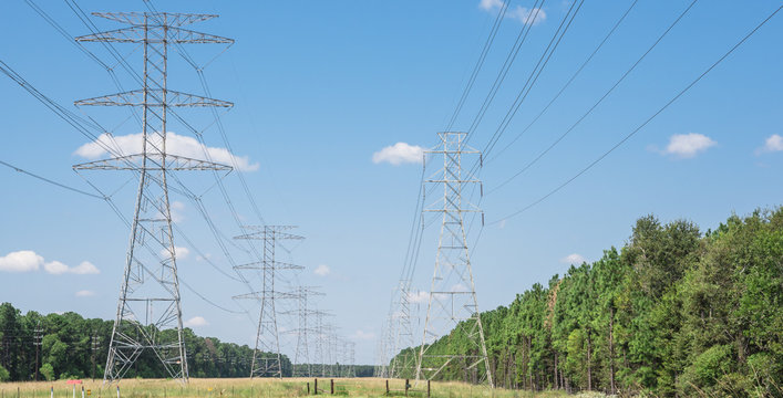 Parallel rows of transmission towers (power tower, electricity pylon, steel lattice tower) cloud blue sky in US. Texture high voltage pillar, overhead power line, industrial background. Panorama style