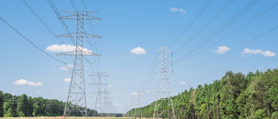 Parallel rows of transmission towers (power tower, electricity pylon, steel lattice tower) cloud blue sky in US. Texture high voltage pillar, overhead power line, industrial background. Panorama style