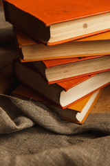 A stack of paper books in orange color on textured wooden surface. Autumn mood concept. Time to read.