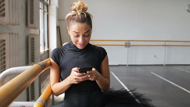 A ballerina uses a smartphone in a large training hall