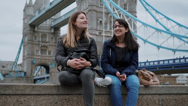 Two friends sit on a wall at Tower Bridge London