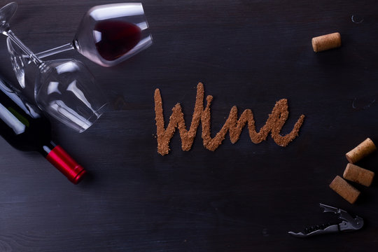 Bottle of red wine and two wine glasses on table with wine word letters