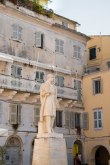 bright sculpture of a male figure standing on a statue on a background of a Mediterranean townhouse with closed shutters