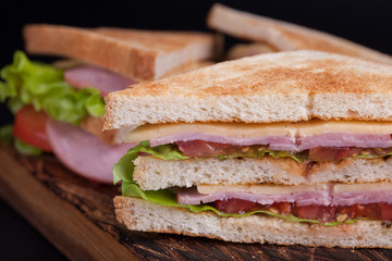 Close-up big sandwich with ham, cheese, tomatoes and salad on toasted bread on a dark background