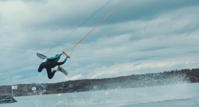 Attractive female practicing wakeboarding tricks in a wakepark near a city. 4K UHD 60 FPS 