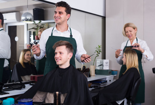 Positive male hairstyler serving teenager in chair