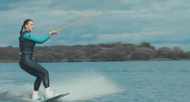 Attractive female practicing wakeboarding tricks in a wakepark near a city. 4K UHD 60 FPS 