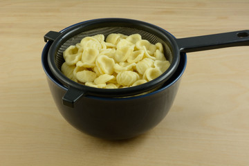 Boiled cooked orecchiette baby ears pasta draining in strainer in blue bowl