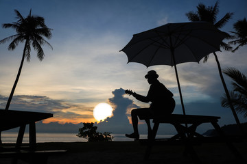 Man playing guitar on the beach with blue sky sunrise