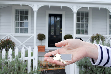Womans hand holds a key against a house in Auckland New Zealand