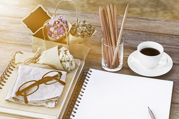 Still life, business, education concept : Close up image open notebook blank pages with glasses, flower bouquet, pencils and coffee cup on wooden table background.