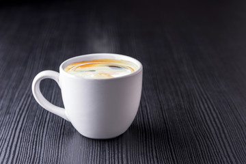 Close up white coffee cup with black espresso on black wood table near window with light shade on tabletop at cafe