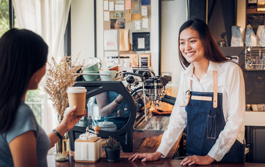 Asian woman barista wear jean apron served to go coffee cup  to customer at bar counter with smile emotion,Cafe restaurant service concept,Owner small business concept