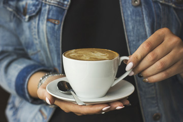 The young woman holding the cup of coffee in her hands