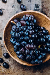 Bunches of fresh ripe red grapes in a wooden bowl on a metal textural surface background. Dark grapes, blue grapes, wine grapes. Copy space