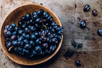 Bunches of fresh ripe red grapes in a wooden bowl on a metal textural surface background. Dark grapes, blue grapes, wine grapes. Copy space