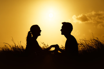 People relationships, love, happy moments. Young couple sitting in a field holding hands talking and enjoying each others company.  