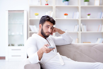 Young man in a bathrobe watching television at home on a sofa co