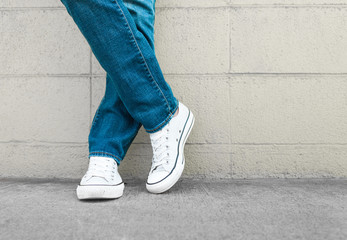 Young person posing in blue jeans and sneakers against brick wall.   Fashion, youth concept.