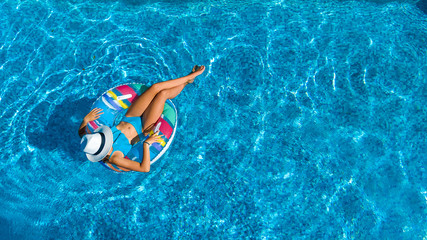 Aerial top view of beautiful girl in swimming pool from above, relax swim on inflatable ring donut and has fun in water on family vacation
