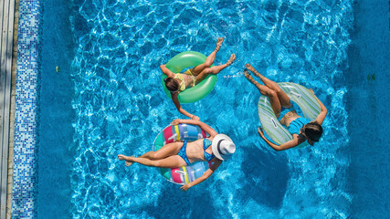 Aerial top view of family in swimming pool from above, happy mother and kids swim on inflatable ring donuts and have fun in water on family vacation
