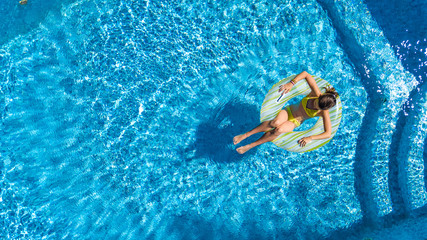 Aerial view of girl in swimming pool from above, kid swim on inflatable ring donut and has fun in water on family vacation
