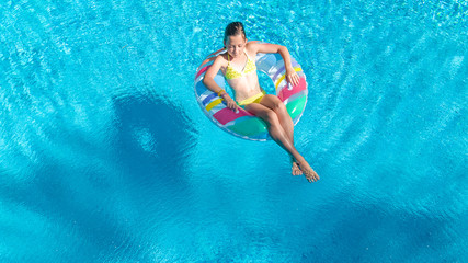 Aerial view of girl in swimming pool from above, kid swim on inflatable ring donut and has fun in water on family vacation
