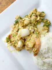 Stir-fried soft-shelled crab in curry and seafood in Curry Powder with thai jasmine rice in white dish on wooden table. (Poo-Pad-Phng-Ka-Ree Thai Food)