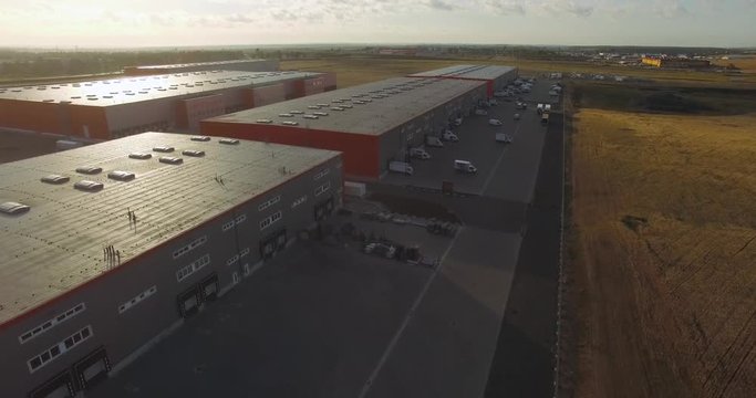 Buildings of logistics center, warehouses in the field near the highway, view from a height, vans and trucks near the warehouse. Aerial view. 

