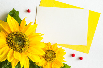 White blank greeting card with big, beautiful yellow sunflowers on the white table. Empty place for a text. Top view.
