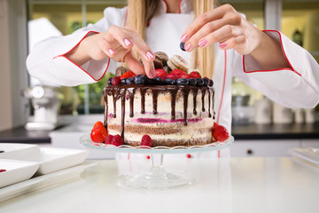 Young female professional baker decorating a chocolate and cream naked cake with blueberries