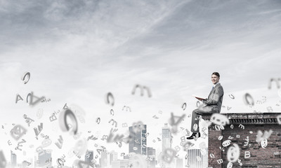 Man on roof edge reading book and symbols flying around