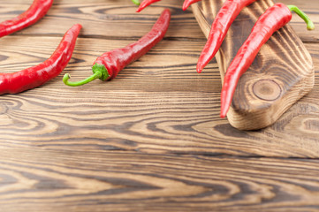Three wholes red fresh ripe chili pepper beside row of pepper on cutting board on old brown wooden rustic planks