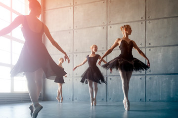 Four beautiful young Russian ballerinas in black packs, white pantyhose and ponts in the style of a black swan dance ballet in a black studio © Виталий Сова