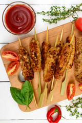 Lula kebab is a traditional Asian dish. Chopped fried meat on skewers. Serve on a board with cereal ciabatta, tomatoes. Top view.