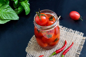 Sour tomatoes in a glass jar on a black background. Pickles