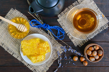 A cup of herbal tea, honey, honeycomb, hazelnuts on a dark wooden background. Healthy foods. Proper nutrition.