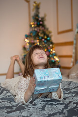 ridiculous funny child with gift  in front of a Christmas tree, golden background,  lifestyle