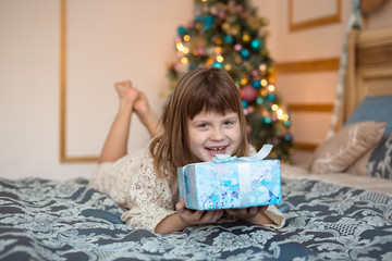 ridiculous funny child with gift  in front of a Christmas tree, golden background,  lifestyle