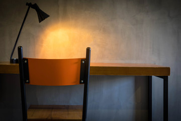 Orange brown chair and table in room with yellow light from lamp and cement wall in the background , dark tone