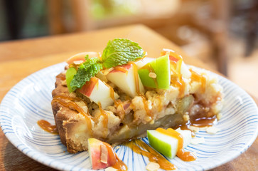 Apple pie with fresh green and red apple and mint on top in ceramic plate on wooden table , warm light
