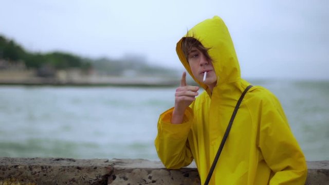 Teenager smoking on shore looks back wind slomo