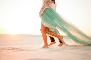 Legs of bride and groom walking barefoot in desert at sunset. Close up.