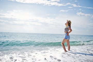 Beautiful model relaxing on a beach of sea, wearing on jeans short, leopard shirt and hat.