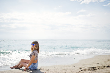 Beautiful model relaxing on a beach of sea, wearing on jeans short, leopard shirt and sunglasses.
