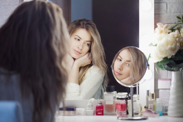 Amazing young woman doing her makeup in front of mirror. Portrait of beautiful girl near cosmetic table