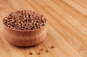 Buckwheat brown in wooden bowl on brown bamboo board, closeup. Healthy dietary groats  background.